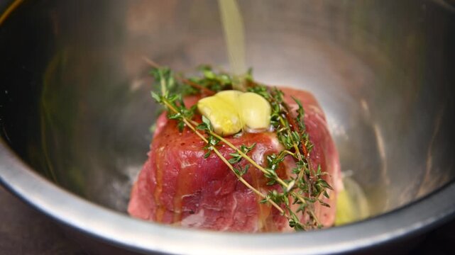 Beef raw steak preparation with garlic and thyme in stainless steel bowl