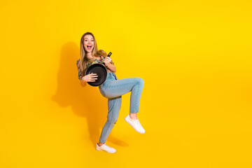 Young woman jumps with a frying pan on a bright yellow background in playful fashion