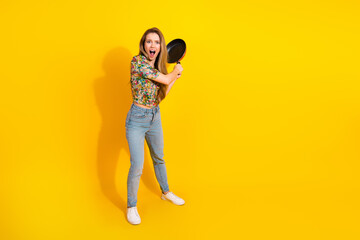 Young woman with frying pan on bright yellow background expresses excitement and fun in a casual...
