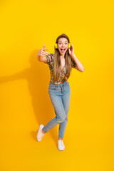 Young woman with yellow headphones enjoys dancing and posing against a bright yellow background in...