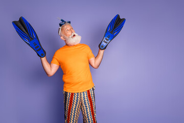 Playful older man with blue fins and orange shirt strikes a carefree pose on a purple background, a humorous, hipster vibe blending fun, fitness, and imagination © deagreez