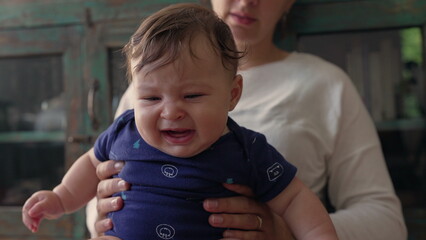 Baby sitting upright in mother’s hands, looking forward with curiosity, engaged and focused, early exploration, childhood discovery, bonding and nurturing moment © Marco