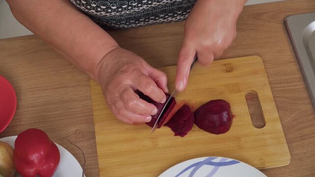 Cutting beetroot into pieces for cooking Ukrainian borscht. Slicing red vegetable for preparing traditional soup. Chopping fresh beet for making borscht recipe. Preparing beetroot chunks for hearty