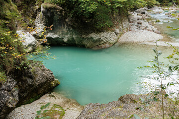 A high-angle view of a clear, turquoise river rushing over smooth stones and boulders, flanked by a steep forested gorge and a wooden boardwalk. Stock photo