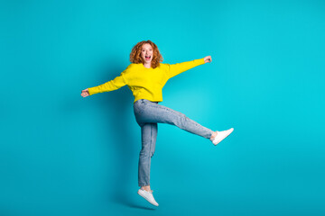 Fototapeta premium Young woman jumping with joy in bright yellow sweater posing against turquoise background
