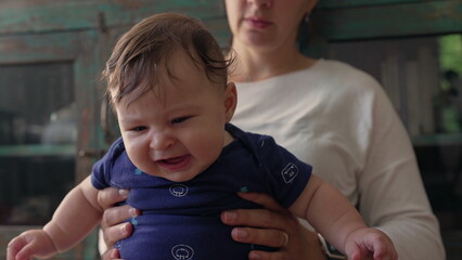 Baby sitting upright in mother’s hands, looking forward with curiosity, engaged and focused, early exploration, childhood discovery, bonding and nurturing moment © Marco