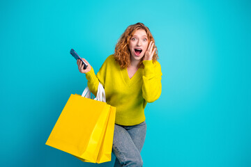 Young redhair woman with yellow shopping bags smiling at camera while holding a remote control in a...