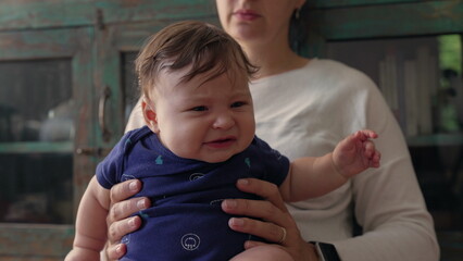 Baby sitting upright in mother’s hands, looking forward with curiosity, engaged and focused, early exploration, childhood discovery, bonding and nurturing moment © Marco