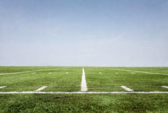 Wide-angle view of green football field near 1-yard line with white hash marks under clear blue sky