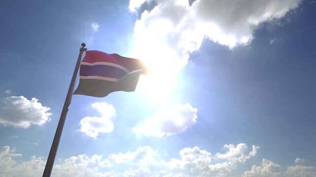 Gambia Flag waving on a Flagpole from a Moving Angle in front of a blue sky with clouds	