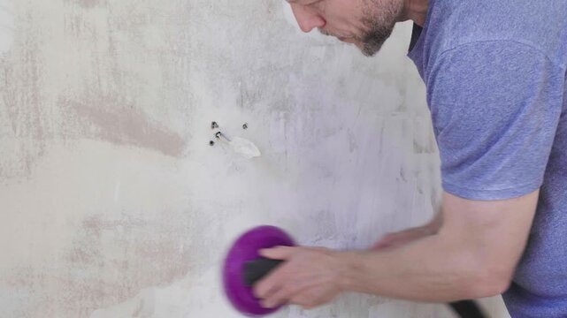 Closeup handyman sanding plaster around electrical outlet with vacuum attachment, brisk lateral strokes, careful clearance of screws and wiring, handson repair
