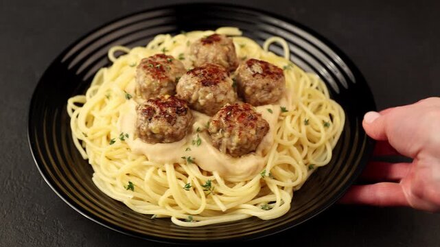 Swedish noisettes (fricandel) with spaghetti and Brune Sos creamy sauce. Traditional meatballs with garnish. Woman turning a plate. Selective focus, close-up.