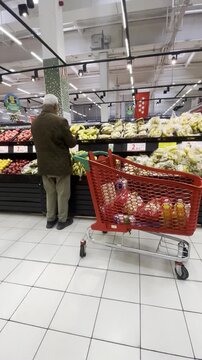 Comprando con carro en s&uacute;per y cesta de mercado en secci&oacute;n fruta en pasillo de hipermercado market