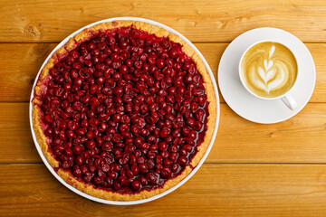 Homemade berry pie with cherry and cup of coffee cappuccino on wooden table. Top view.