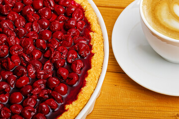 Clodeup homemade berry pie with cherry and cup of coffee cappuccino on wooden table.