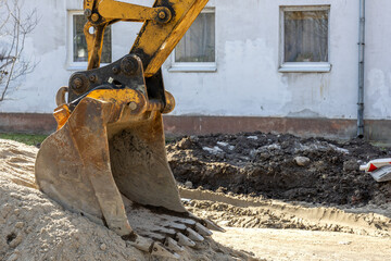 Fototapeta premium Excavator bucket digging trench during urban construction and infrastructure repair