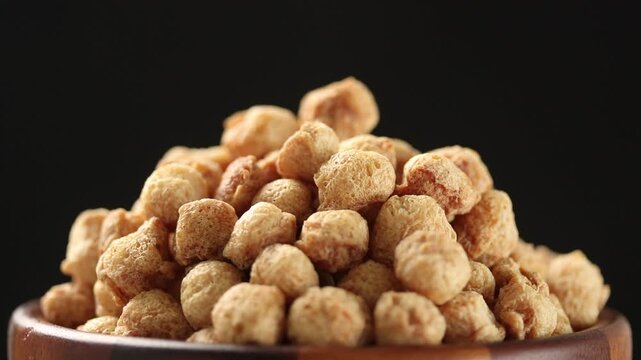 Slowly rotating dry textured vegetable protein (TVP) or soy meat in wooden bowl on black background. a plant-based meat substitute