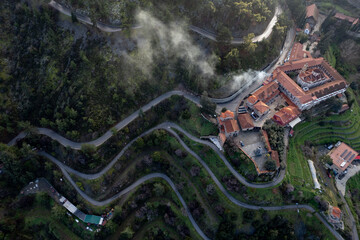Panagia Machaira christian monastery complex on a mountain slope in troodos, cyprus, during sunrise, with fog and smoke rising from the hills