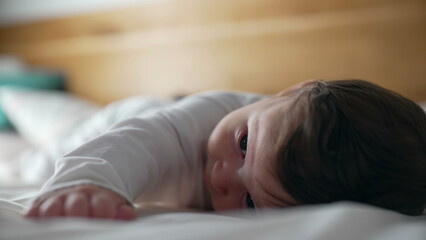 Baby lying on stomach, playful expression, smiling while lifting head, early development, tummy time, strengthening muscles, childhood curiosity, joyful moment, home setting