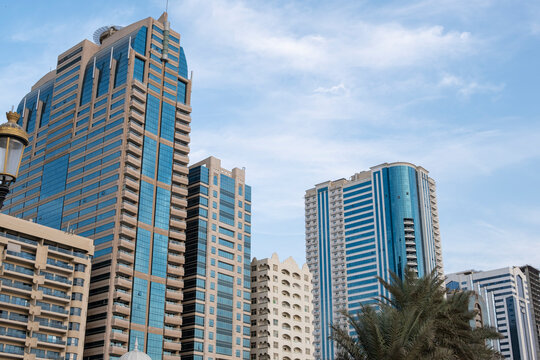 12.12.2025 Sharjah, UAE. Panoramic view of Sharjah Corniche at sunset, featuring Khalid Lagoon water, illuminated skyscrapers, modern city skyline, and silhouette of date palm trees in UAE