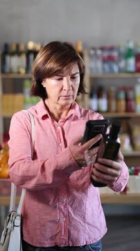 Female buyer checks suitability - scans QR code on olive oil label in a grocery store. High quality 4k footage