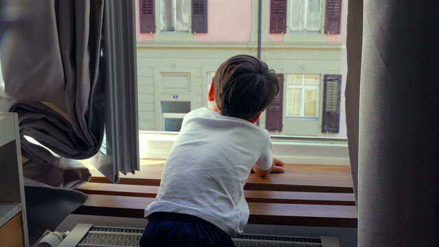 Young boy leaning on windowsill, gazing outside, deep in thought, quiet moment of reflection, childhood curiosity, urban home setting, observing city life, daydreaming
