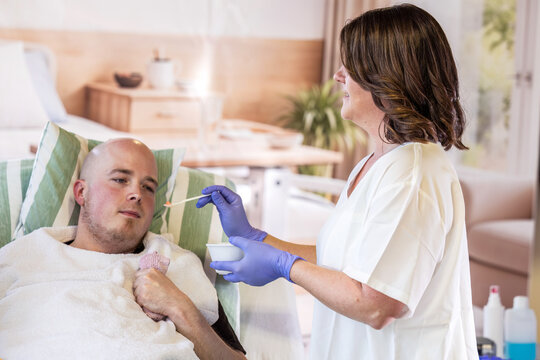 Young male patient with spastic contracture receiving assisted feeding from nurse during hospital nursing care