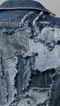 Vertical video: Tilting camera revealing distressed denim jacket back on plain wall, showing seams