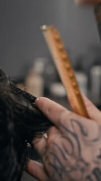 Vertical close up of unrecognizable barber using scissors and comb while styling dark male hair