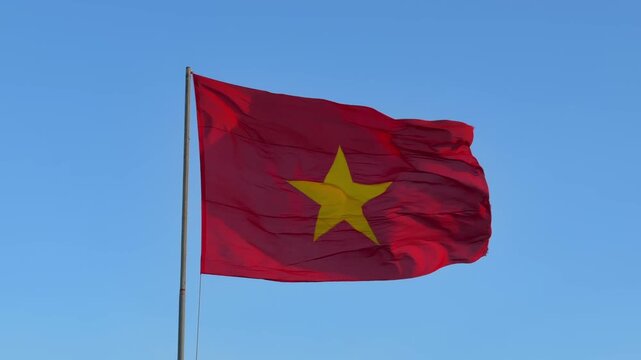 Vietnam flag in slow motion moves on a tall flagpole, reacting to wind under warm sunset sky and calm evening light above the horizon. National pride.