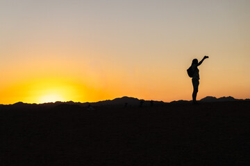 Traveler silhouette taking selfie at desert sunset in Egypt with mountains on horizon