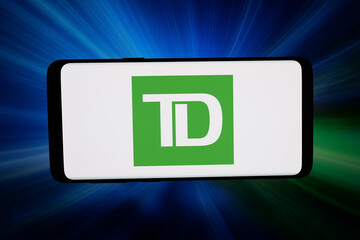 Naklejka premium Stuttgart, Germany - 03-04-2026: In this photo illustration, the logo of company Toronto-Dominion Bank (TD Bank Group) is displayed on a smartphone in front of abstract background on computer screen.