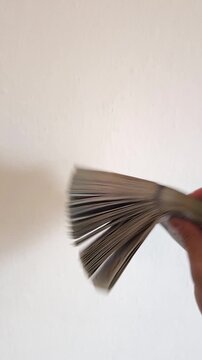 Caucasian hand showing thick pack of US dollars on white background.
