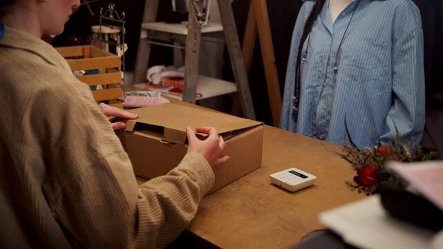 Small business owner packing clothing order and handing parcel to customer at shop counter