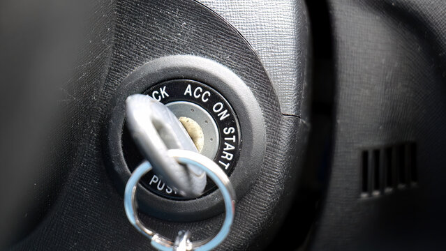 Car key inserted in ignition switch closeup detail shot, vehicle dashboard lock accessory on start position, parked automobile interior macro detail, transport security and driving concept, no people