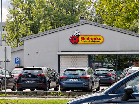 Cars parked in front of Biedronka supermarket building in Krakow Poland, grocery store entrance and parking lot with Polish brand sign, urban daily life retail shopping concept, no people