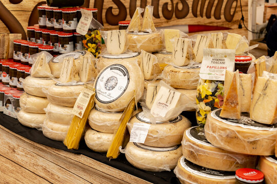 Assorted vacuum packed artisan cheese wheels, wedges and pasta on a rustic market stall counter, gourmet delicatessen display with truffle varieties, jars and Italian specialty foods