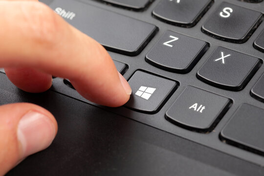 Finger pressing Windows 10 key on black laptop keyboard, closeup of Microsoft logo shortcut button, operating system end of support EOL updates security patches concept, work from home IT maintenance