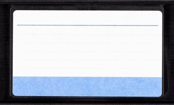 Blank VHS cassette label with blue lined sticker on black videotape cartridge, front view closeup isolated on white background, 80s 90s retro analog home video archive mockup template with copy space