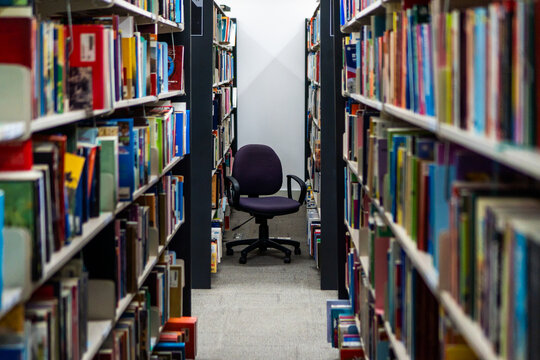 Empty office chair at the end of a library aisle with colorful books for education and study concepts.