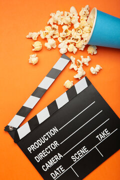 A clapper and a bucket of delicious salted popcorn on orange background. Vertical photo