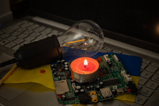 Energy crisis in Ukraine: candlelight on motherboard and laptop with ukrainian flag