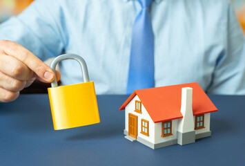 A house and a padlock in a man's hand. Ensuring property safety and home protection. Security...