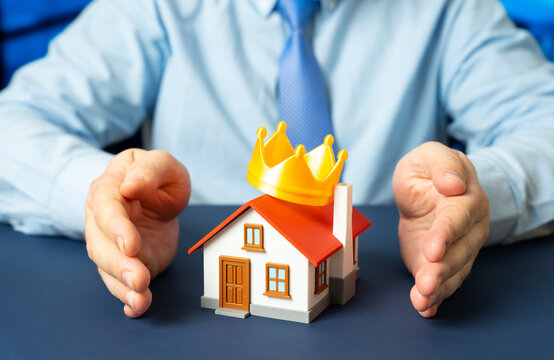 A man clasps his hands around a house with a crown on the roof. Property insurance and protection of valuable homes. Premium housing, buying and renting real estate and the idea of the perfect home.