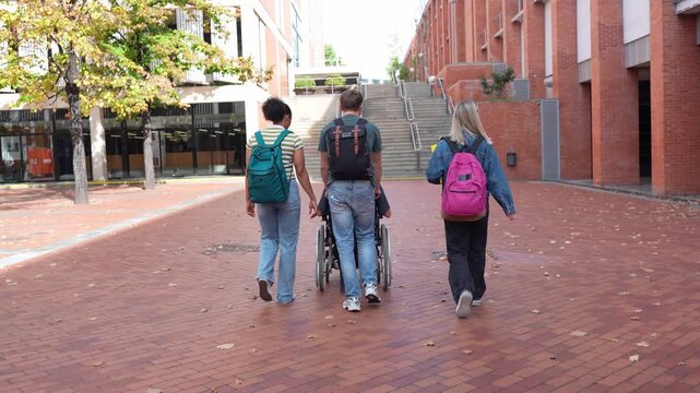 Inclusive group of university students walking together. One student in a wheelchair being pushed by a friend on the brick paved campus