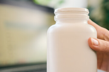 Closeup of female hand holding bottle of vitamins for beauty and health care. Hand holding white plastic supplement bottle, closeup of container for vitamins or medicine