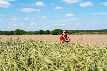 Fototapeta premium Female farmer talking on mobile phone near wheat field during growth season.