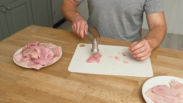 Person using meat tenderizer on raw chicken. Chef preparing pork loin slice with meat mallet on cutting board. Man tenderizing fillet. Cooking cutlets pounding poultry breast close-up. Culinary dish.