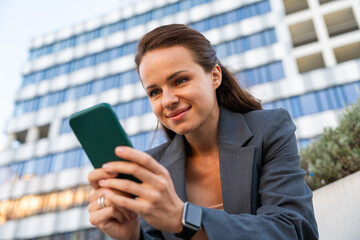 Fototapeta premium Modern businesswoman using her smartphone outdoors on city street.