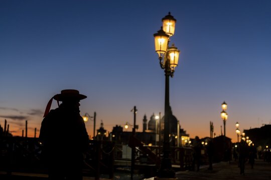 Gloomy atmosphere, gondolier as silhouette at blue hour in front of illuminated street lamp, Venice, Veneto, Italy